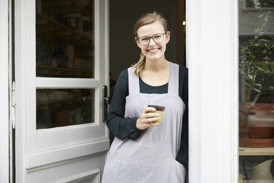 Portrait of confident female owner having coffee at doorway of art studio