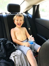 Portrait of shirtless boy holding bottle while traveling in car