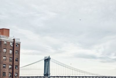 Suspension bridge in city against cloudy sky