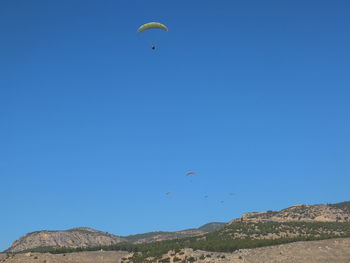 Low angle view of people paragliding against clear blue sky