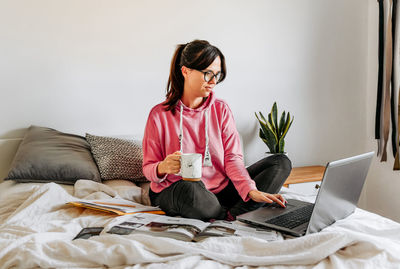 Young woman, student, sitting on bed, studying for exams, laptop, book.