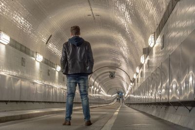 Rear view of man standing in illuminated tunnel