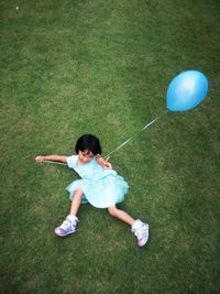 Portrait of smiling girl lying on field while holding balloon