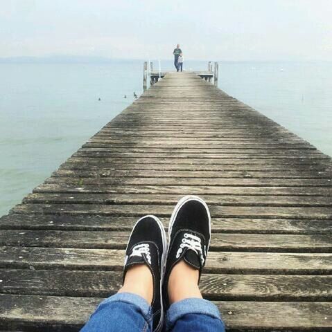 low section, water, pier, person, wood - material, lifestyles, men, boardwalk, standing, personal perspective, leisure activity, shoe, sea, unrecognizable person, railing, sky, lake, nature