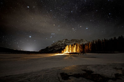 Night shot mountain, lit trees and frozen lake, banf