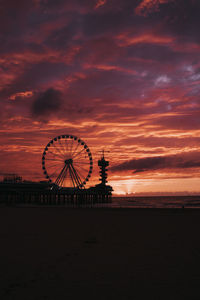 Silhouette ferris wheel by sea against orange sky