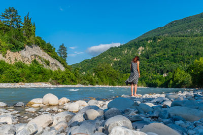 Rear view of woman standing on rocks against blue sky