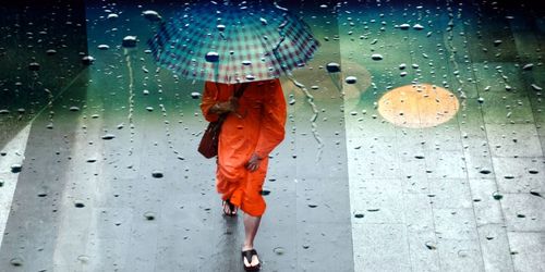 Double exposure of wet glass and monk walking with umbrella during rainy season