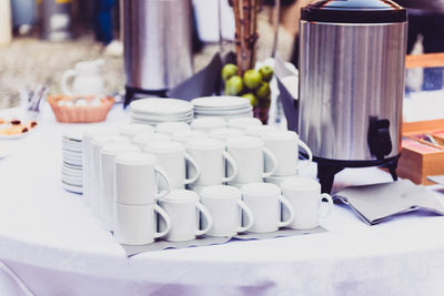 Close-up of stacked cups by container on buffet table