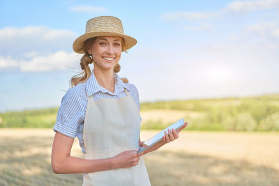 Portrait of smiling young woman wearing hat standing on field