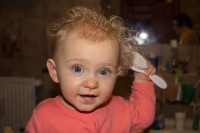 Portrait of cute girl combing hair with brush at home