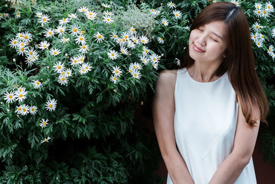 Portrait of young asian woman standing amidst flowering daisy plants on field.