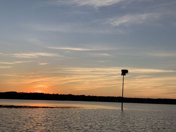 Silhouette street by lake against sky during sunset