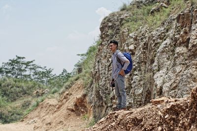 Young man standing on rock against sky