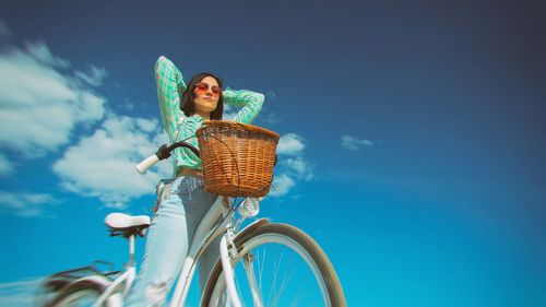 Low angle view of young woman with bicycle against sky