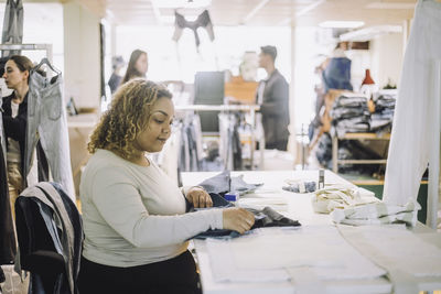 Side view of young female fashion designer examining fabric while working at workshop