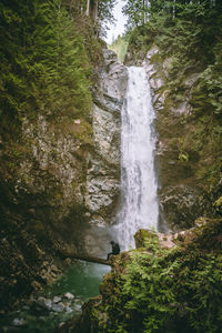 Man sitting on mountain against waterfall in forest