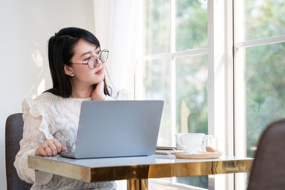 Young woman using mobile phone while sitting on table