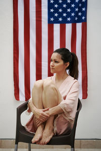 A young girl sitting with the american flag in the background. concept of america