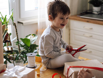 Cute smiling boy holding scissors sitting at home