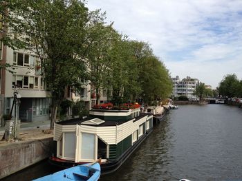 Canal amidst trees in city against sky