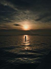 Silhouette person in sea against sky during sunset