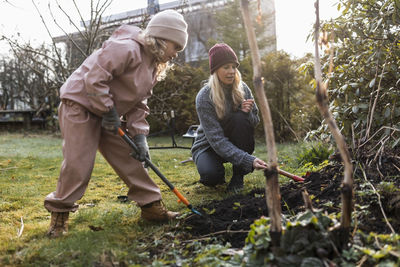 Full length of mother and daughter digging with shovel while doing gardening at back yard