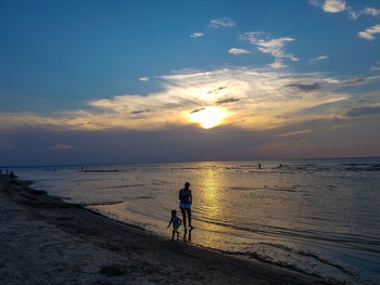 People on beach against sky during sunset