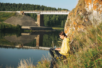 Side view of man sitting on bridge over lake