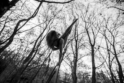 Low angle view of woman pole dancing against bare trees in forest