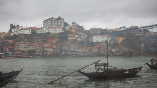 Sailboats in river by buildings in city against sky