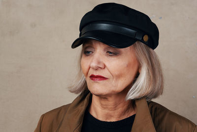 Senior woman wearing cap against wall