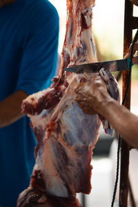 A man with a knife is cuttting the meat hanging on the hook.