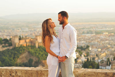 Side view of young romantic couple standing by retaining wall