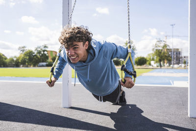 Happy sportsman exercising with suspension straps at sport court