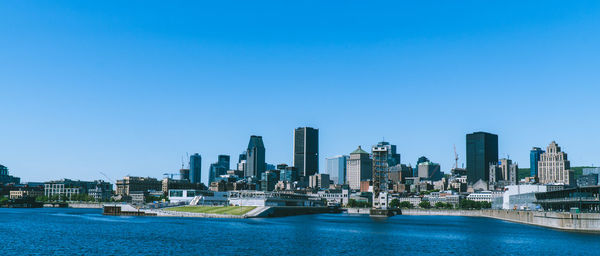 Scenic view of river by buildings against clear blue sky