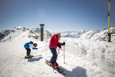 Full length of brother and sister skiing against clear sky