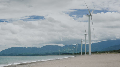 Scenic view of sea, mountains and wind turbine