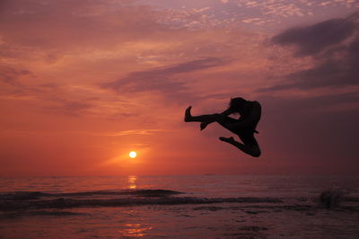 Silhouette man dancing at beach against sky during sunset