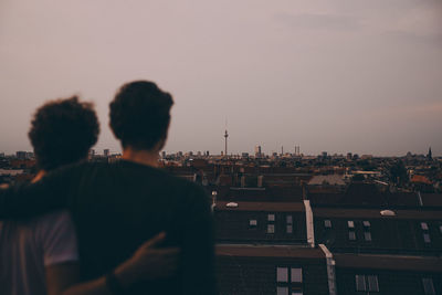 Rear view of male friends with arms around looking at city while standing on terrace during party