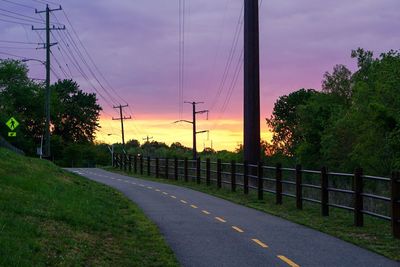 Road by trees against sky during sunset