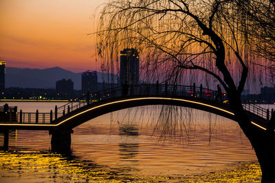 Silhouette bridge over river against sky at sunset
