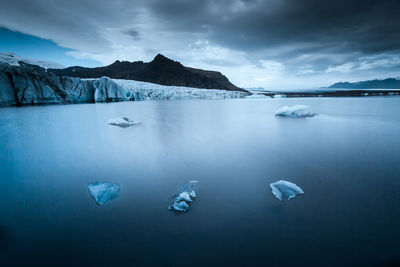 Iceberg floating in sea against sky at dusk