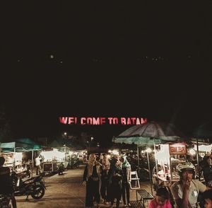 People on illuminated street against sky at night