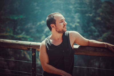 Young man looking away while standing against railing