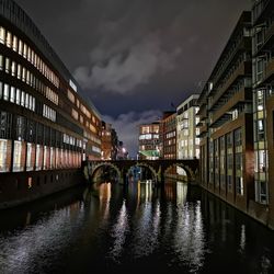 Bridge over river amidst buildings in city at dusk