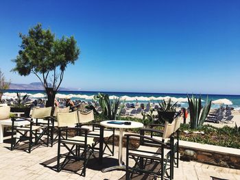 Empty chairs and table at beach against clear blue sky