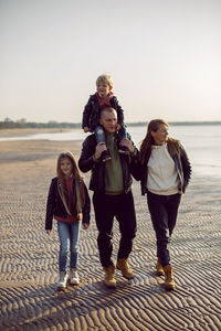 Family in a leather jacket walks along the beach with their dog in autumn