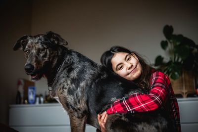 Smiling girl in checked pajama hugs her grey dog