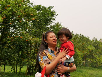 Mother holding daughter outdoors while standing against trees